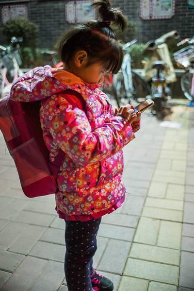 1月19日,在济南实验初中校门外,一位和姑姑来等表姐放学的小女孩,背着幼儿园的小书包,站在那里低头聚精会神地玩着姑姑的手机。视觉中国供图(资料图片)