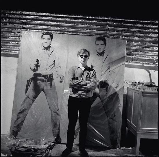 艺术品:© 2018The Andy Warhol Foundation for the Visual Arts, Inc。 / Licensed by Artists Rights Society (ARS),照片:© Bruce Davidson/Magnum Photos。 安迪-沃霍尔与《双面猫王》 于工作室的合影,约1964年