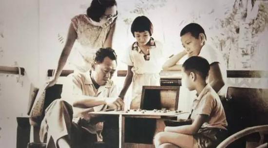 一家五口围在一个棋盘周围,李光耀与儿子上演“父子战”。(网络图)