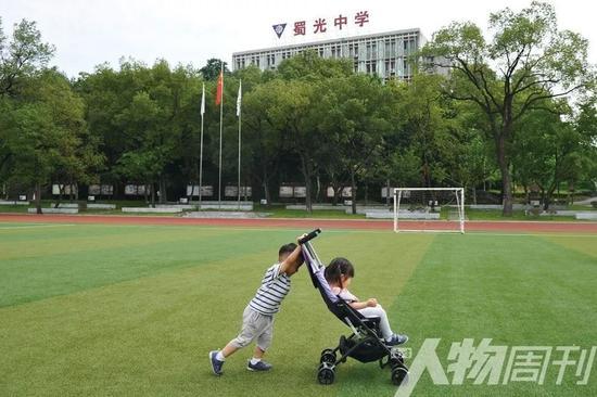 四川自贡,一个男孩推着坐在儿童推车上的妹妹在校园里玩耍