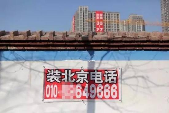 河北燕郊入口处的建筑工地外墙上贴着装北京电话的广告。图/CFP