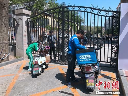 2017年4月21日,北京交通大学南门附近,由于快递电动车无法进入校园,一名学生隔着铁门取外卖。潘心怡 摄