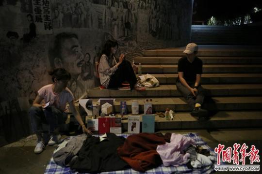 6月19日晚,中央美术学院,硕士毕业生钟钰炜(左一)与朋友在跳蚤市场上摆摊,身后的壁画描绘了央美百年历史。中国青年报·中国青年网见习记者 孔斯琪/摄