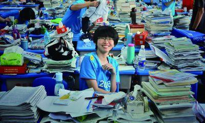 考后,一名学生坐在成堆的复习材料中面对镜头微笑