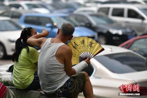 资料图:7月11日,成都气温突破35℃。当日,成都市气象台对10日发布的今年首个高温橙色预警信号进行了第一次确认。图为一老人在停车场为小女孩扇风拭汗。 张浪 摄