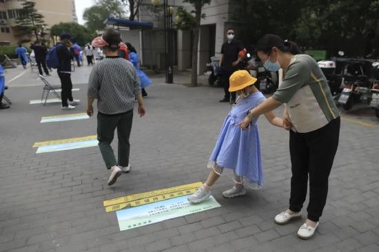 ▲5月5日,海淀区羊坊店街道莲花小区,一位检测完核酸的妈妈带着女儿在读地上的古诗。 新京报记者 浦峰 摄