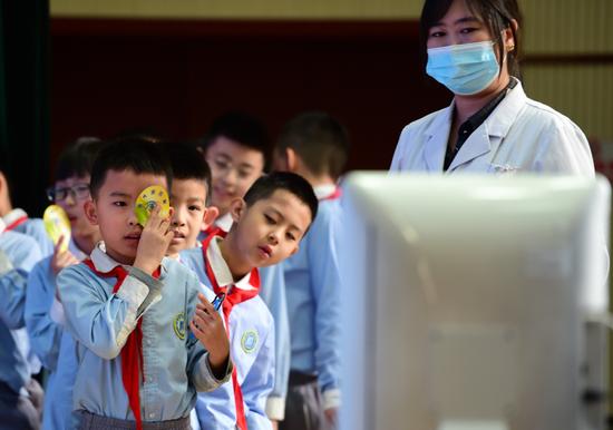 2021年3月22日,在河北沧州市实验小学,医生志愿者指导学生进行裸眼视力检查。新华社发(傅新春 摄)
