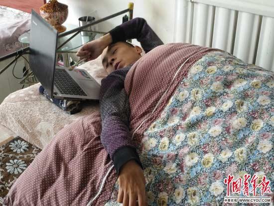 在家中的床上,都海成手握铅笔,用笔头敲电脑键盘进行文学创作。 中国青年报·中青在线记者 马富春 图