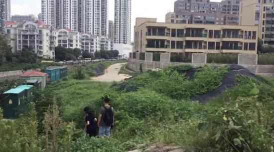 幼儿园位于小区西南角,围墙下道路与幼儿园有3米落差,如今道路施工,人只能翻过荒草一米高的小山坡到达幼儿园。