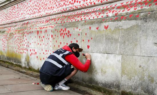A volunteer paints red hearts representing the victims who died of COVID-19 on the National COVID Memorial Wall outside St Thomas' Hospital in London, Britain, on March 31, 2021. (Xinhua/Han Yan)