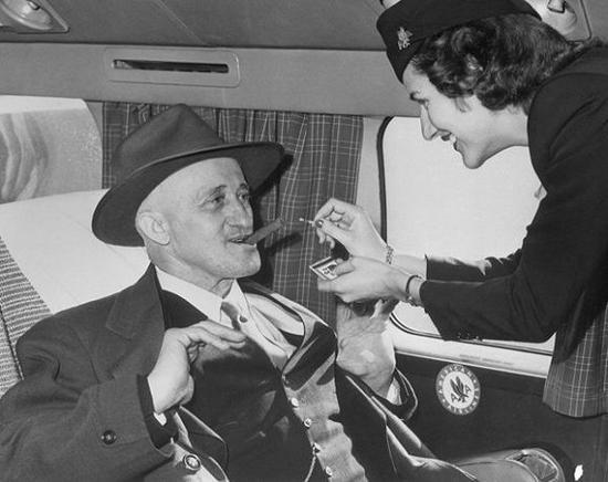 1949年11月10日,东圣路易斯航空公司空姐Jane Driscoll为68岁的Carl Graulein点雪茄。