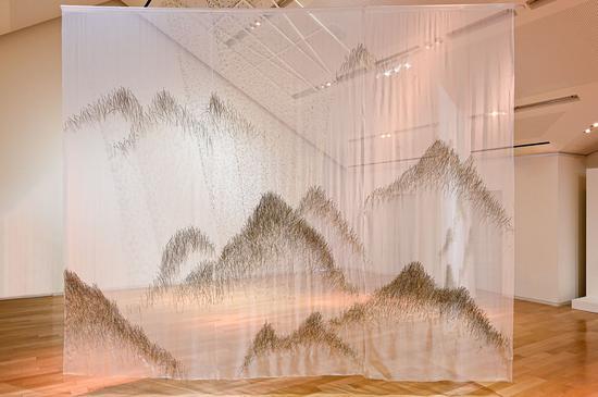 上海“爱马仕之家”《梦之秘境》艺术展——装置《松山》以取自大自然的松针在层层薄纱上编织成图案,营造出雾中远山的景象。