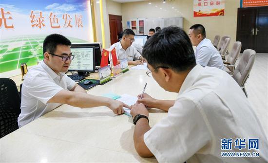 7月16日,在内蒙古自治区自然资源厅的自然资源政务大厅内,办事员(左)为采矿企业办理相关审批手续。新华社记者 彭源 摄