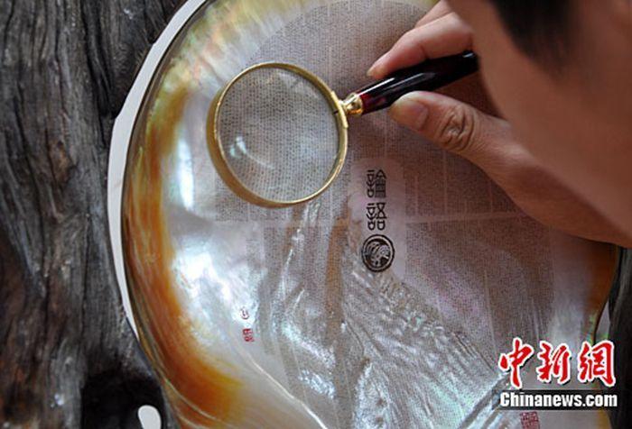 资料图:此前,在广西南宁举行的首届广西工艺美术作品展暨工艺美术大师精品展上,广西工艺美术大师利成世的作品《论语明珠》吸引观众用放大镜观看,该作品将1.5万多字的《论语》全文微刻在一枚珍珠贝母上,行楷字体纤毫毕现。中新社发 刘万强 摄