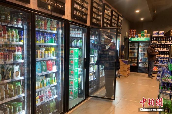 当地时间7月22日,南非约翰内斯堡,一家酒类商店的店员佩戴面罩整理冰箱内的货物。 中新社记者 王曦 摄