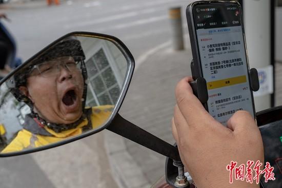 9月2日,北京,常凯在路边等红绿灯的时候一边刷单一边打着哈欠。为了给骑手提供“24小时服务”,他平时睡在“小哥加油站”里的一张简易折叠床上,有时候要忙到后半夜。