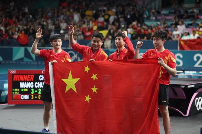 图为比赛胜利后,樊振东(左一)、马龙(右二)、王楚钦(右一)和教练王皓(左二)手持五星红旗在场内庆祝夺冠。
