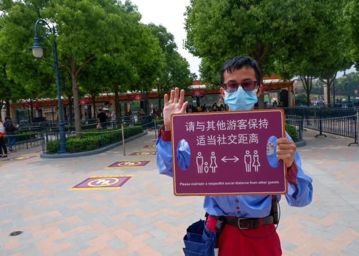 迪士尼园区内,随处可见举着标识牌的工作人员,提醒游客之间保持社交距离。