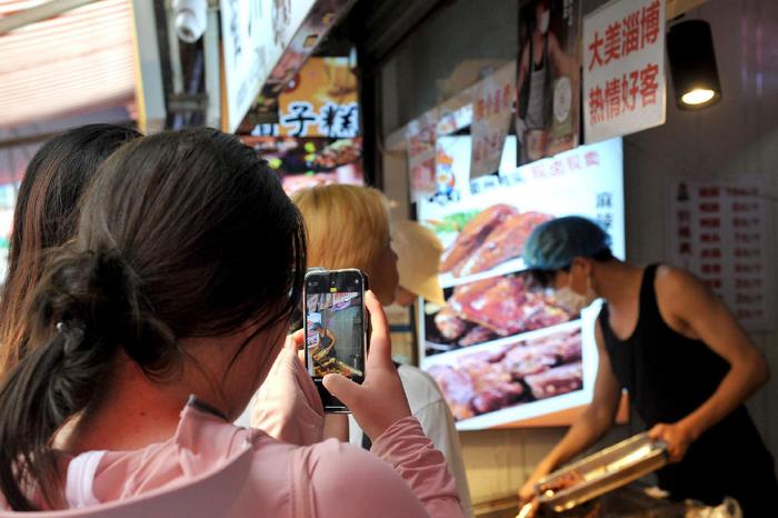 ▲今年6月,“鸭头小哥”在店里忙碌时有顾客拍照围观。图据视觉中国