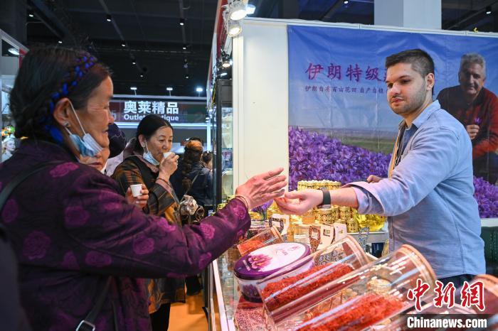图为拉萨进口商品展览会现场,伊朗商人(右)向顾客品尝藏红花。中新社记者 贡嘎来松 摄