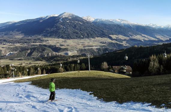 奥地利一处雪场，一名滑雪者站在少量人造雪覆盖的雪道边缘