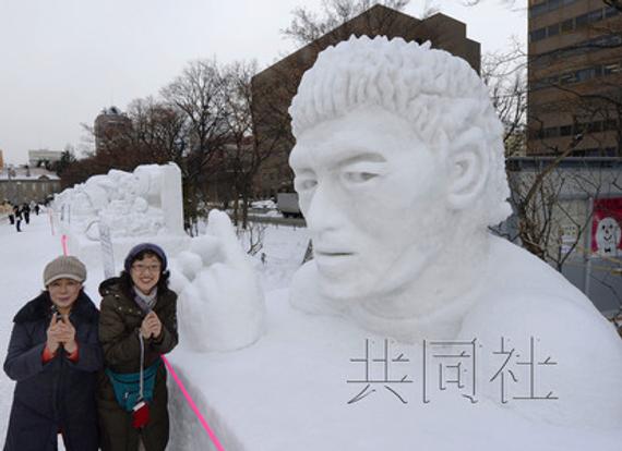 女游客在札幌大通公园内的橄榄球运动员五郎丸步雪雕前合影留念。（共同社）