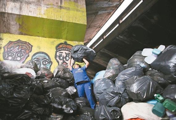 图为巴西圣保罗市一名垃圾收集员高举大袋垃圾堆放。 路透