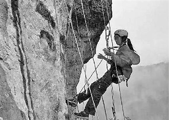 女子吊着绳索在岩壁上作画