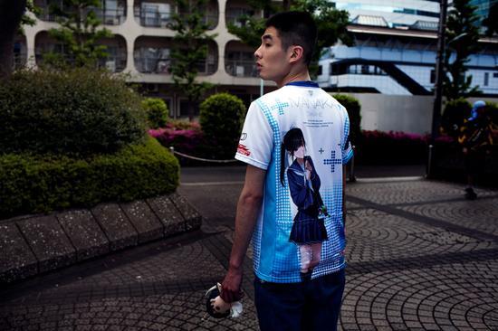 25岁的《爱相随》玩家Naoki是一名火车站警卫。他身穿印有爱花的T恤,手里拿着她的手办。图片来源:LOULOU D’AKI