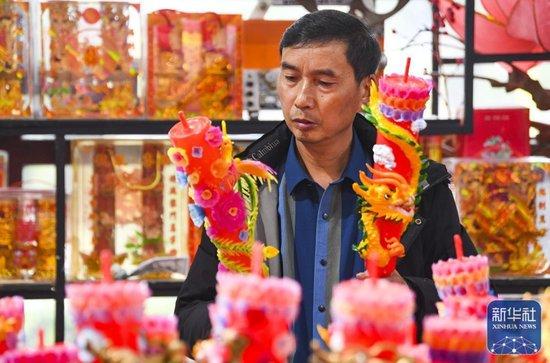 ↑1月25日,陈建友在工作坊查看龙凤花烛产品。