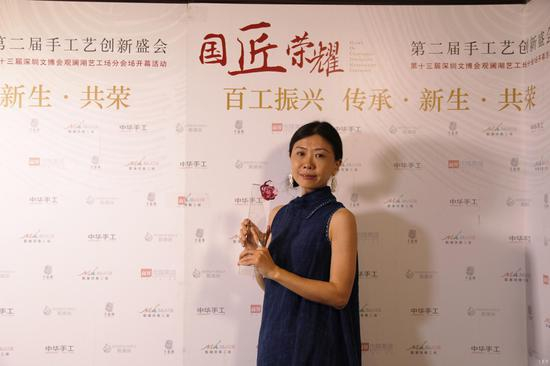 蕊工坊创始人谢晓蕊在活动现场接受采访时，与中国振兴传统工艺百强企业奖杯合影