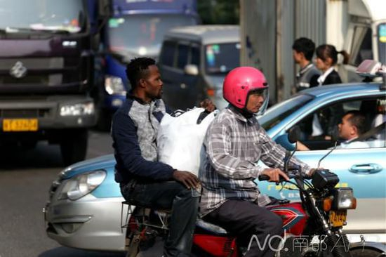 石井一个服装批发市场外，一名外籍男子抱着货物搭乘出租摩托车。