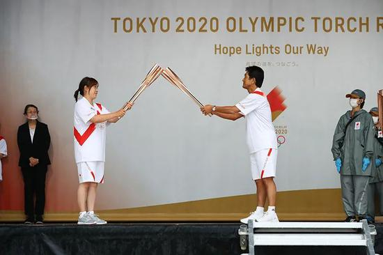　　2021年5月12日，日本福冈县北九州市，前日本女排运动员竹下佳江（左前）和前日本网球运动员、东京奥运会日本代表团团长福井烈（右前）在点火仪式舞台上交接火炬。图|新华社