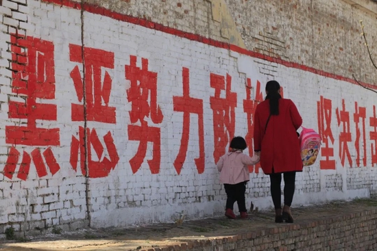 2018年4月7日，河南安阳，一名妇女拉着孩子在标语前走过。