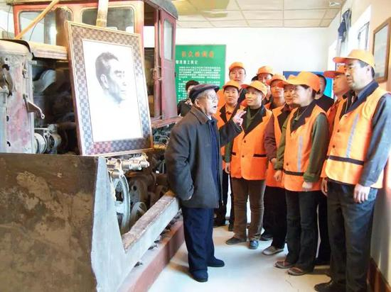 张富贵（左一）为青年职工介绍周恩来总理向十工道班赠送“东方红75 型推土机”的故事。