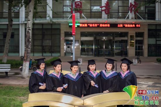 毕业女学员的背后是我院图书馆，象征知识与能力，她们聚集在书的雕塑前面，聚精会神的看着，重温那段遨游书海、挑灯夜战的辛勤岁月，她们必将秉承勤学苦练的拼搏精神，回到部队，必将为中国梦、强军梦添砖加瓦、铺路搭桥。中国青年网通讯员 褚龙 摄