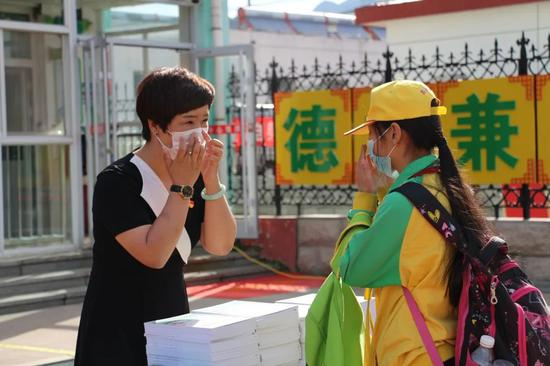 在学校门口，王春艳校长为每个返校的学生赠送健康礼包，并为孩子演示正确佩戴口罩的方式。