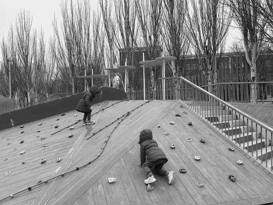 西红门口袋公园地面上散落着垃圾。孩子在无人打扫的攀爬坡上玩耍，老人跟着给孩子拍灰。