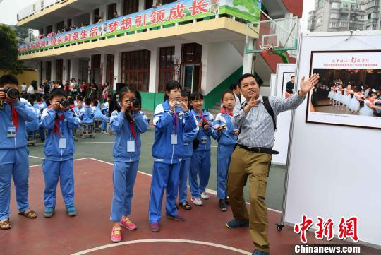 图为5月31日，摄影希望小学摄影小社团的学生拿着爱心相机在摄影师的指导下学习拍摄。　张斌 摄