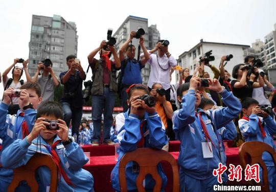 图为5月31日，摄影希望小学摄影小社团的学生拿着爱心相机和摄影家们一起在校园摄影学校“六一”节活动。　张斌 摄