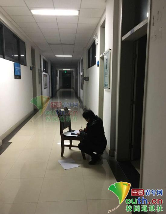 图为冉春芳在走廊借光蹲着批阅试卷。学校官微供图