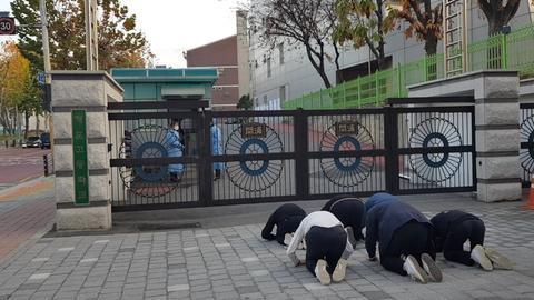 11月17日,韩国数名高中生在高考考场前磕头应援。(纽西斯通讯社)