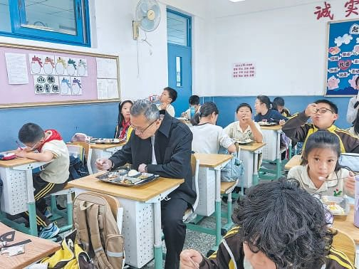 育翔小学校长王春伟（中）在教室里陪餐。本报记者 李祺瑶 摄