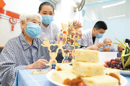  ▲日前，北京市隆福医院天通苑院区举办“喜迎国庆、重阳敬老”主题活动。住院的老年人在医护人员的陪护下一起搭九九重阳塔、品重阳糕，体验钓螃蟹、五官拼贴、手指舞蹈等趣味游戏，娱乐的同时还锻炼了手眼肢体协调能力。北京日报记者 方非摄