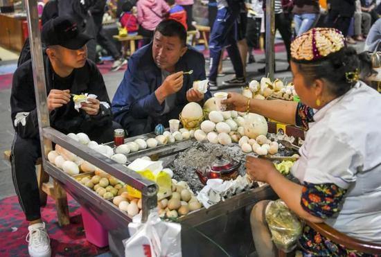 新疆和田夜市：游客品尝炭火烤蛋。中新社记者 刘新 摄