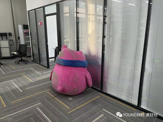 ‘深受员工喜爱’的吉祥物YOYO，被丢弃在地上，沾满尘土，它附近‘每日优鲜便利购’办公室中仍有人开会
