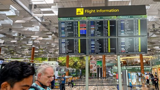  2025 年 3 月 21 日，在新加坡樟宜机场，人们走过显示新加坡航空公司飞往伦敦希思罗机场的 SQ318 航班已取消的离港信息板。