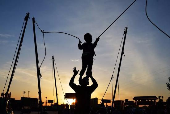 河北雄安新区容城县三贤广场上，一家长正托举着孩子玩蹦床。图 / 视觉中国