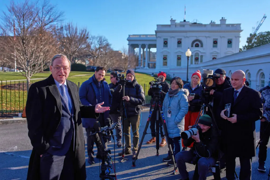凯文・哈塞特身着黑色长款大衣，在白宫背景前接受记者群访。这位白宫国家经济委员会主任认为，人工智能将赋能人力而非取代人力，其角色无异于一位‘金牌教练’。