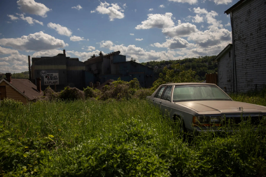  一辆老旧汽车被杂草环绕，背景是工业建筑。这是宾夕法尼亚州布拉多克的一家钢铁厂。研究人员发现，北美自由贸易协定加速了美国制造业的衰退。